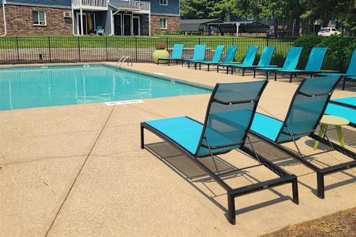 A pool with blue chairs and a bench.
