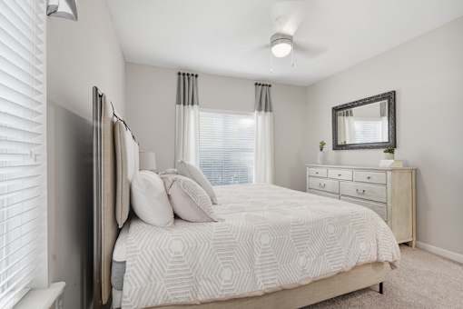 A bedroom with a bed, dresser, and window with blinds.