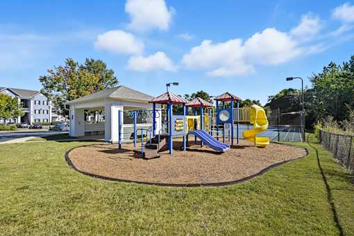 A playground with a yellow slide and a white building.
