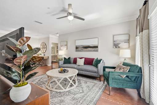A living room with a grey couch, a green armchair, a coffee table, and a plant in a white vase.