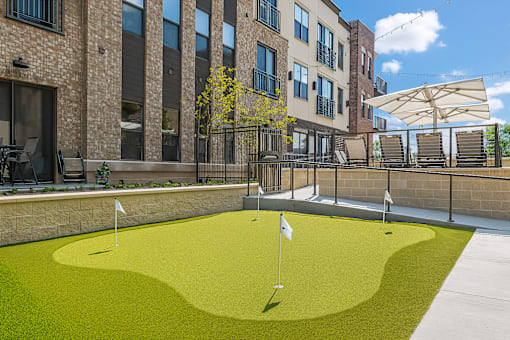 A small putting green is surrounded by a brick building.