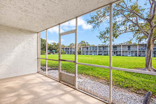 A room with a view of a grassy area and a building through the window.