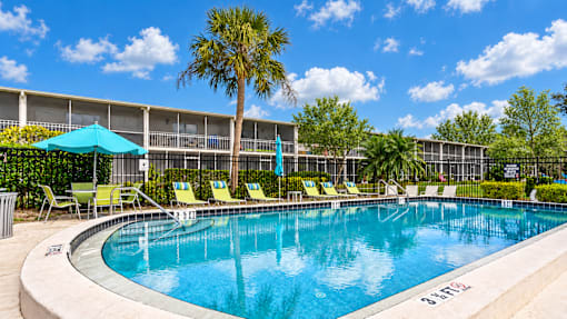 Swimming pool with lounge chairs, turquoise umbrellas and palm trees at Waterchase Apartments in Largo, FL.