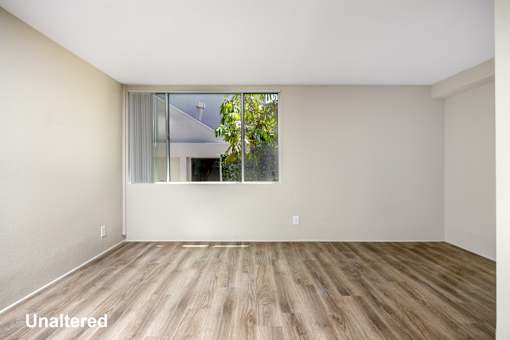 A room with wooden flooring and a window showing trees outside.
