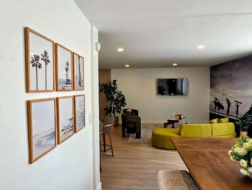 A living room with a yellow couch and a painting of a palm tree on the wall.