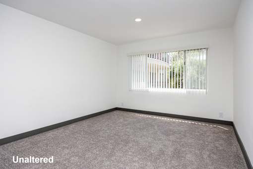 A room with unaltered carpeting and a window with blinds.