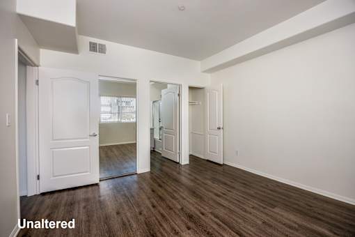 A room with white walls and wooden floors with a door on the left.