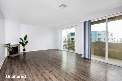 A room with unaltered wooden flooring and a fireplace with a plant beside it.