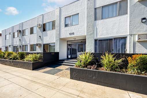 an apartment building with a sidewalk and plants in front of it