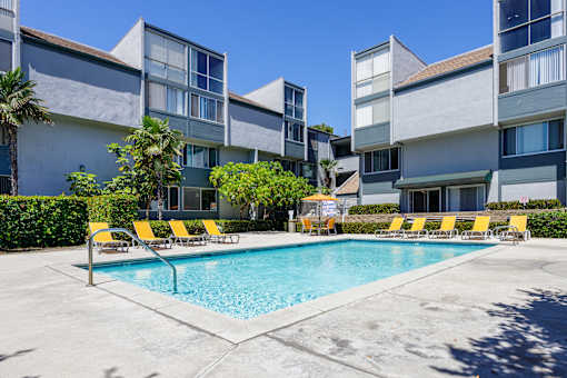 a swimming pool with yellow chairs in front of an apartment building