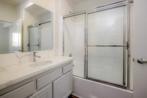 A white bathroom with a sink, mirror, and shower.