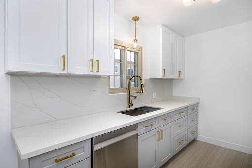a kitchen with white cabinets and a sink and a gold faucet