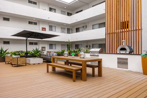 A wooden table with chairs and a black umbrella in the middle of a wooden deck.