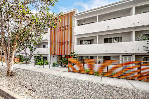 A modern building with a white and brown facade is surrounded by a gravel area and a wooden fence.