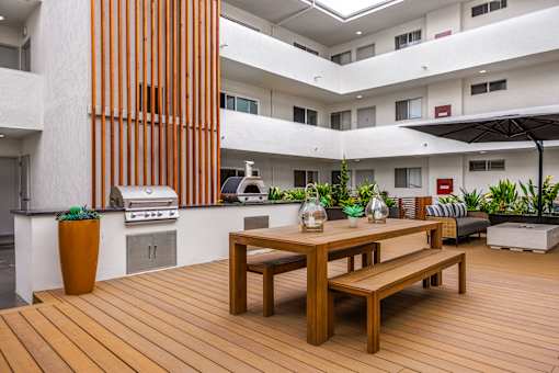 A wooden table and bench are in the foreground of a modern patio area.