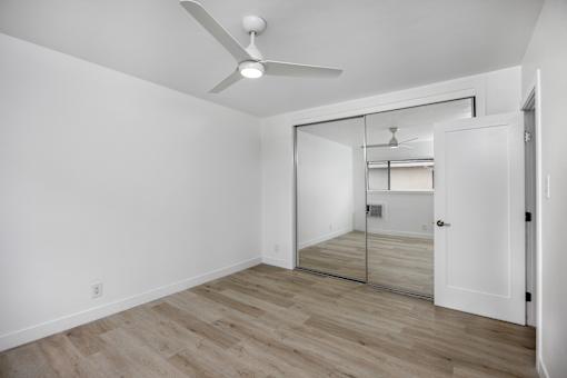 A room with a ceiling fan and a mirrored doorway leading to another room.