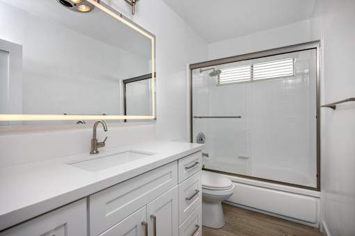 A white bathroom with a sink, mirror, and toilet.
