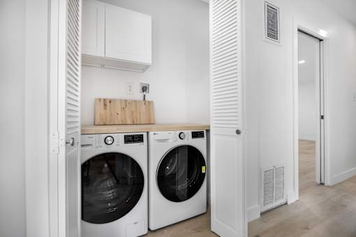 A white laundry room with two washing machines and a wooden board on top of the dryer.