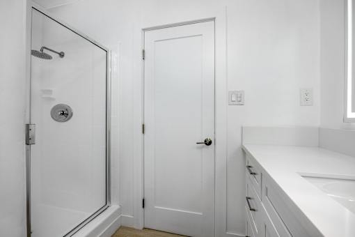 A white bathroom with a door, a shower, and a sink.