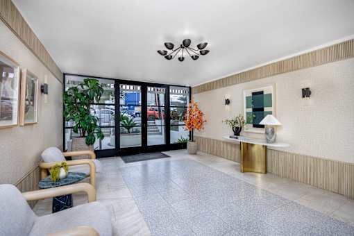 A well-lit waiting area with a bench, a table with a lamp, and a window with a view of the outside.