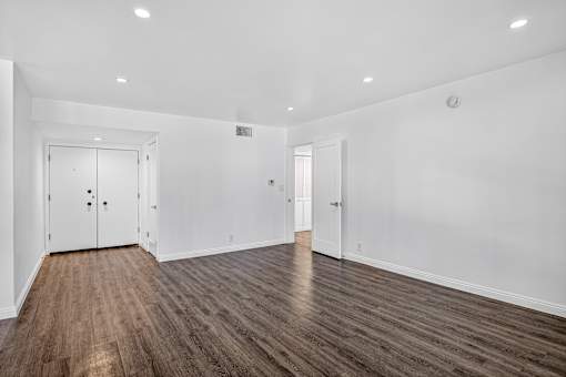A room with white walls and wooden flooring with a door on the left side.
