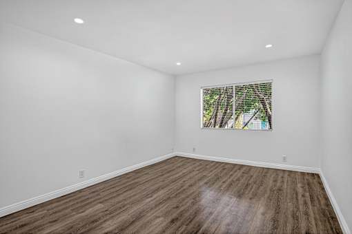 A room with wooden flooring and a window with a view of trees.