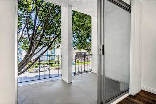 A glass door opens to a balcony with a tree in the background.