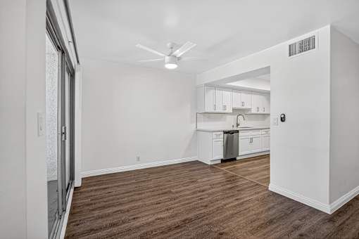 A room with a ceiling fan and a kitchen area in the background.