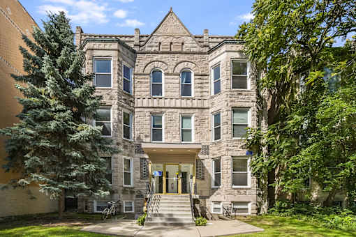 A large, historic-looking building with a front porch and a tree in front.