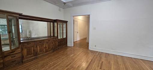 A room with wooden floors and white walls, with a cabinet and a doorway visible.