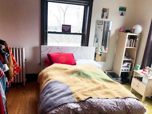 A bedroom with a bed, a bookshelf, and a window with a sign that says "MERCHANDISE ONLY".