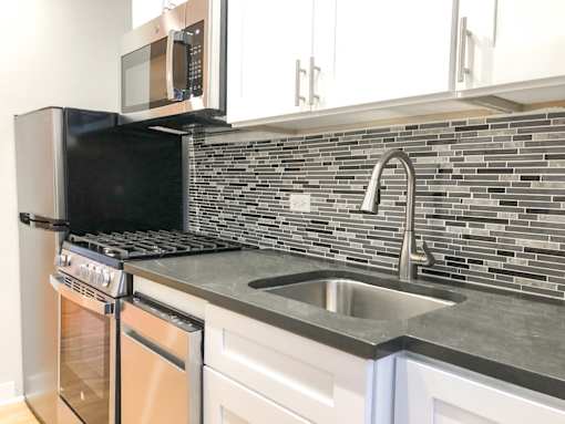 A kitchen with a black microwave above a stove and a silver sink.