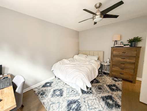 A bedroom with a bed, a dresser, a ceiling fan, and a rug.