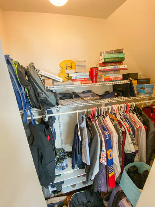A cluttered closet with clothes and books on top.