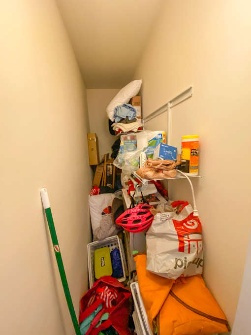 A small, narrow hallway is filled with various items, including a mop, bags, and boxes.