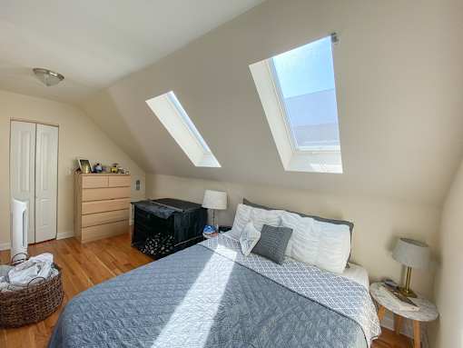A bedroom with a bed, nightstand, and a window with skylights.