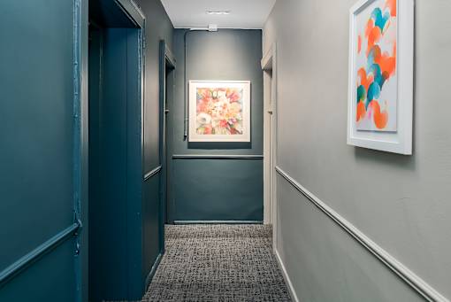 A hallway with a painting on the wall and a carpeted floor.