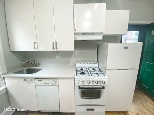 A white kitchen with a stove, sink, and cabinets.