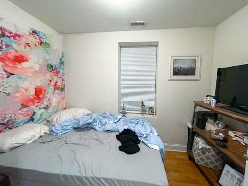 A bedroom with a bed, a TV, and a window with blinds.