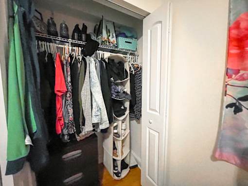 A white closet with clothes hanging on a rail.