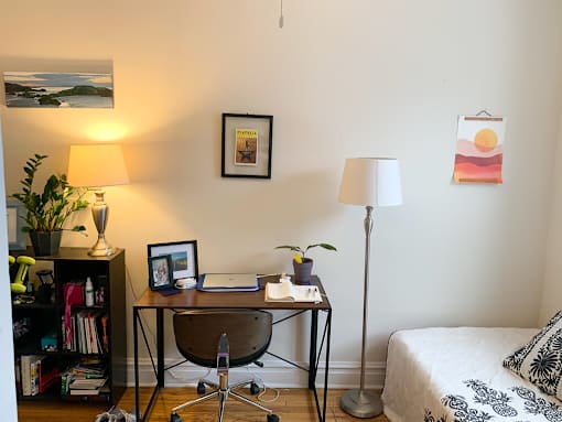 A room with a bed, desk, chair, and a lamp.