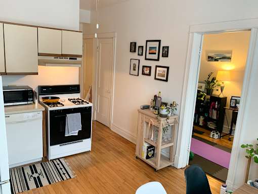 A kitchen with a white oven and microwave, a wooden floor, and a white chair.