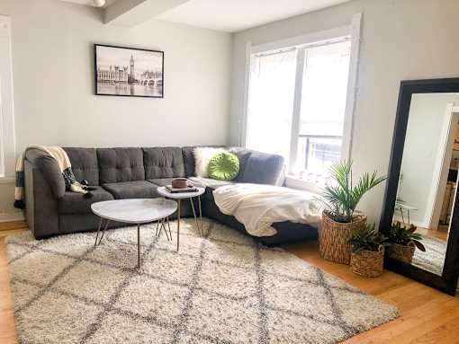 A living room with a grey sofa, a white bed, and a large mirror.