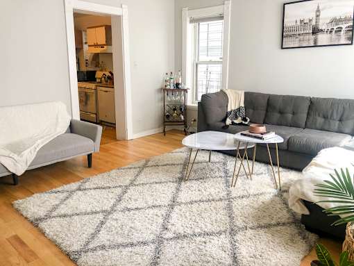 A grey couch sits in a living room with a white rug in front of it.