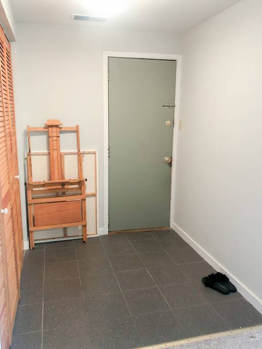 A room with a green door and a wooden shelf.