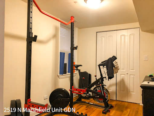 A home gym with a squat rack, a weight bench, a barbell and a weighted wheel.
