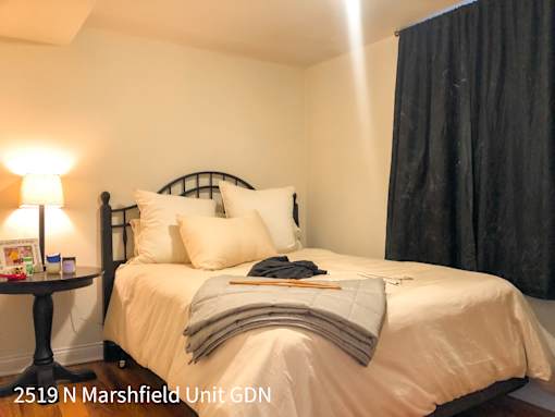 A bedroom with a bed, pillows, a nightstand, and a lamp.