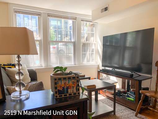 A living room with a couch, a chair, a table, a lamp, a plant, a picture frame, a television, and a book.