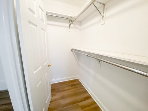 a walk in closet with white walls and a wood floor