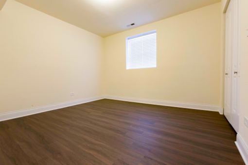 A room with wooden flooring and a window with blinds.